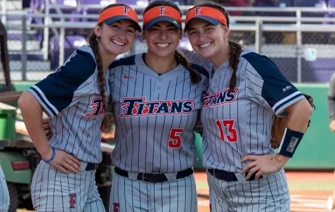 Three softball players smiling in uniforms.
